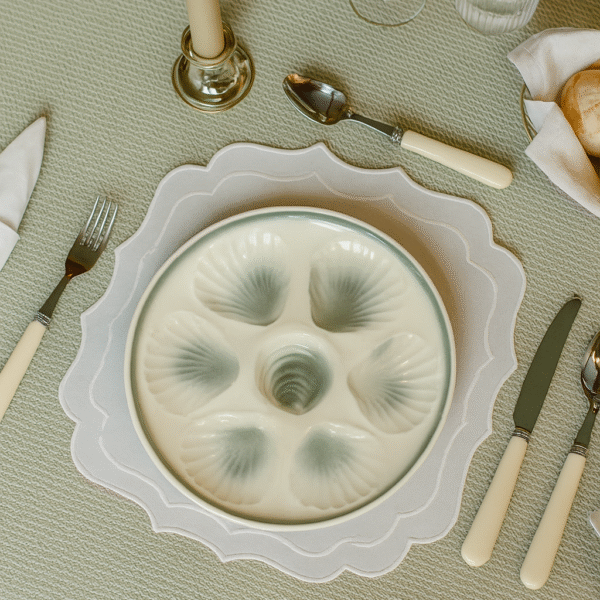 White and grey oyster plate placed on a set table that has a green tablecloth, knife, fork, spoon, glasses and a cangle