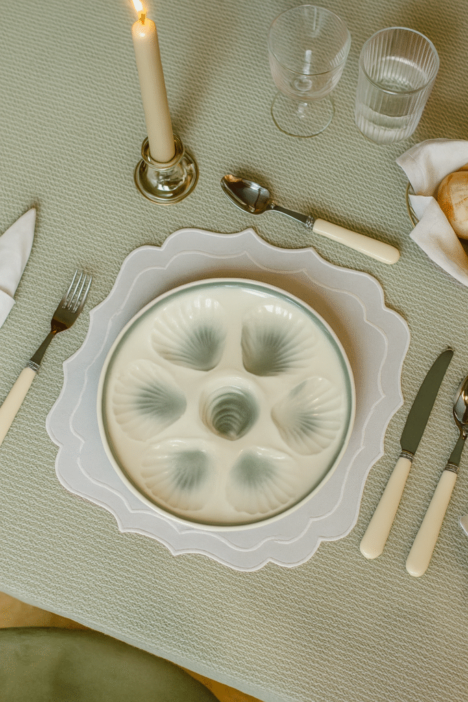 White and grey oyster plate placed on a set table that has a green tablecloth, knife, fork, spoon, glasses and a cangle